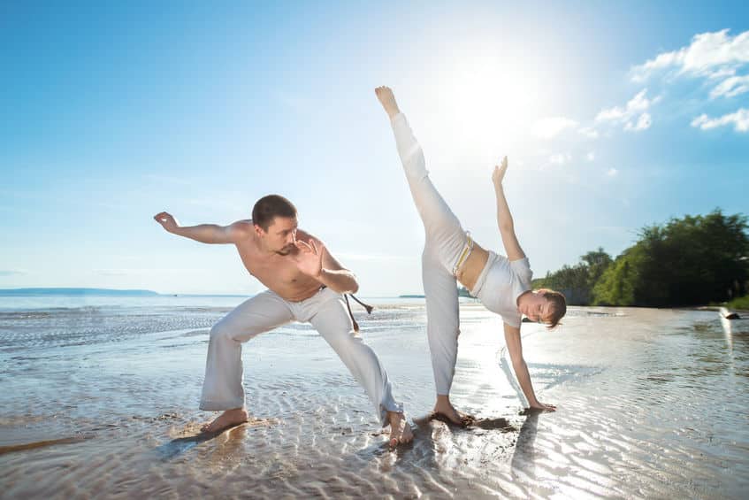 a man and a woman train capoeira on the beach.